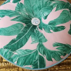 a decorative green and pink plate with leaves on it, sitting on a gold table