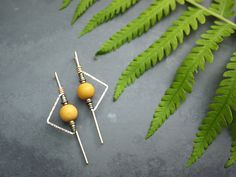 two yellow beads sitting on top of each other in front of a green fern leaf