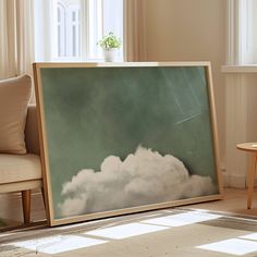 a painting is sitting on the floor in front of a chair and table with a potted plant