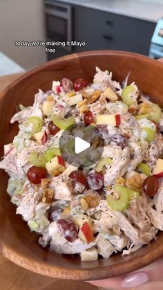 a person holding a wooden bowl filled with fruit and chicken salad on top of a table