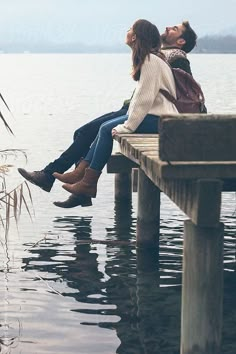 two people are sitting on a dock by the water