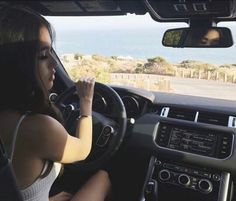 a woman sitting in the driver's seat of a car with her hand on the steering wheel