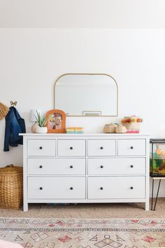 a white dresser sitting next to a wall with a mirror on top of it in a room