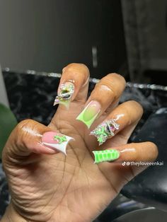 a woman's hand with green and white nail polish on it, holding up her nails