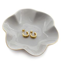 two gold - plated earrings on a white flower shaped dish