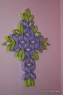 a cross made out of paper with green leaves on the top and purple petals on the bottom