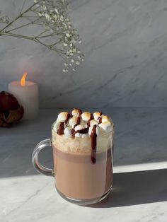 there is a cup of hot chocolate with marshmallows on it and a candle in the background