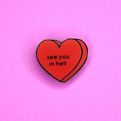 a red heart shaped pin with the words see you in hell on it against a pink background