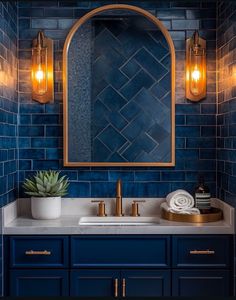 a bathroom with blue tile and gold accents, including a mirror over the sink that has lights on it