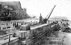 an old black and white photo of people standing on the side of a road next to a body of water