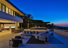 an outdoor living area with couches, tables and chairs on the patio at dusk