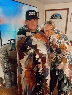 a man and woman standing in front of a flat screen tv holding a blanket over their shoulders