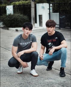 two young men are sitting on the sidewalk and one is wearing a black t - shirt