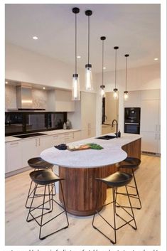 an island in the middle of a kitchen with stools and lights hanging from it