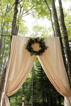 an outdoor wedding ceremony with white drapes and greenery on the top, surrounded by tall trees