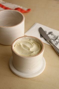 two white cups with cream sitting on top of a table