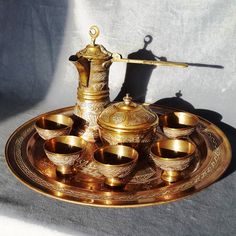 an antique brass tea set on a tray with cups and saucers in front of it