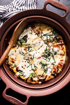 a pizza with cheese and herbs in a brown casserole dish next to a wooden spoon