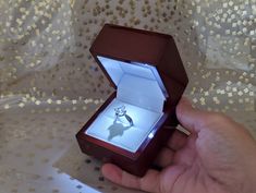 a hand holding an open ring box with a diamond in it