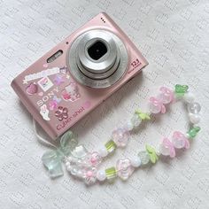 a pink camera sitting on top of a table next to a beaded necklace and lanyard