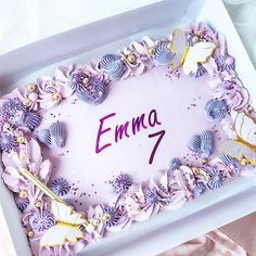 a birthday cake with purple frosting and flowers in a box that says emma 7