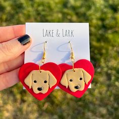 a pair of red heart shaped earrings with a dog's face on it, sitting in front of a card