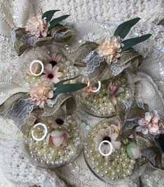 three small glass vases with flowers and pearls on the bottom are sitting on a lace doily