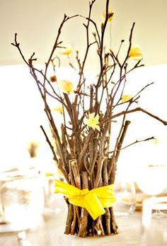 a vase filled with branches and flowers on top of a wooden table covered in yellow ribbon