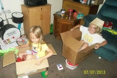 two children sitting in cardboard boxes on the floor