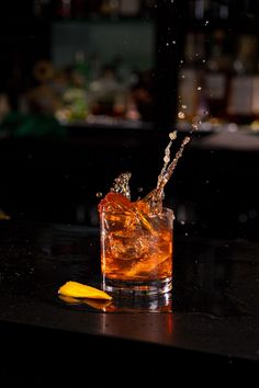 an alcoholic drink being poured into a glass with ice and lemon wedges on the table