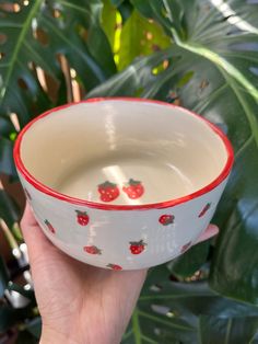 a hand holding a white and red bowl with strawberries painted on it's sides