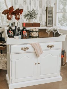 a white dresser with bottles and glasses on it