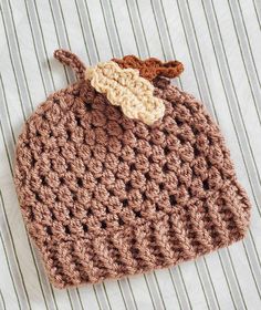 a crocheted brown hat with a leaf on it sitting on a striped cloth