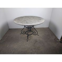 a white marble top table with wrought iron legs in an empty room next to a wall