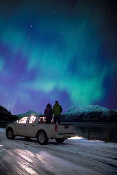 two people standing on the back of a pick up truck in front of an aurora display