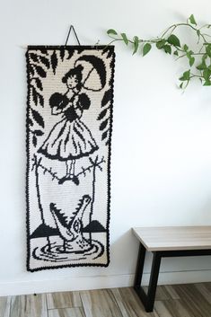 a crocheted wall hanging next to a wooden bench and table with a potted plant on it