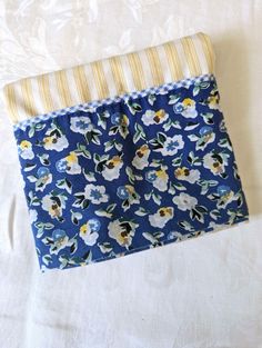 a blue and white flowered cloth with yellow stripes on it, sitting on a bed