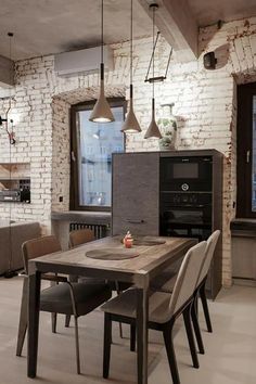 a dining room table and chairs in front of a brick wall with exposed lights hanging from the ceiling