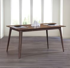 a wooden table with two plates on it in front of white walls and wood flooring