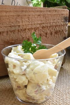 a glass bowl filled with potato salad next to a wooden spoon