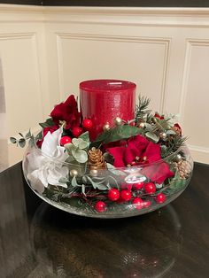 a glass bowl filled with red flowers and greenery on top of a wooden table