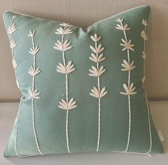 a green pillow with white flowers on the front and back, sitting on a couch