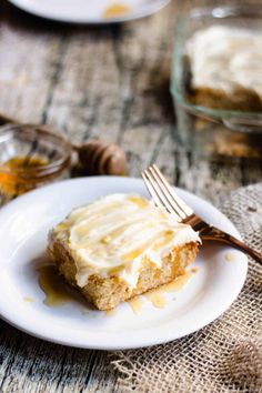 a piece of cake on a white plate with a fork and honey in the background