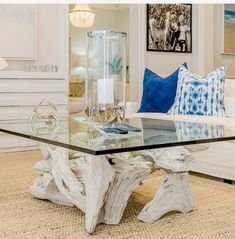 a glass table with white driftwood and blue pillows