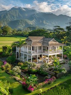 a large white house surrounded by lush greenery and mountains in the background with trees