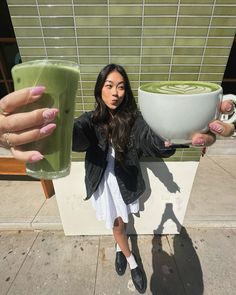 a woman holding up two large cups with green liquid in them while another person holds out their hands