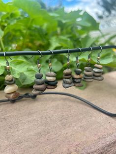 several small rocks are hanging from a metal bar with ear wires attached to them, along with green plants in the background