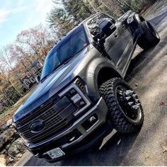 a black truck parked on the side of a road next to some trees and bushes