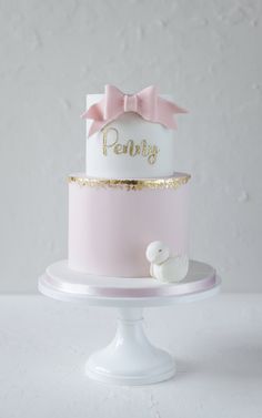 a pink and white cake with a bow on top is sitting on a pedestal in front of a wall