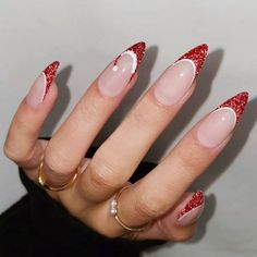 a woman's hand with red and white nail polish on her nails, wearing gold rings